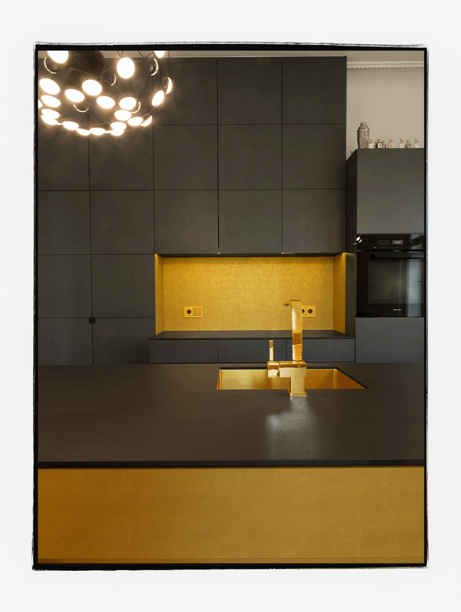Küche mit goldfarbiger Kochinsel und einer Arbeitsplatte aus Keramik, im Hintergrund ein Hochschrank aus anthrazitgrauen Eternitplatten